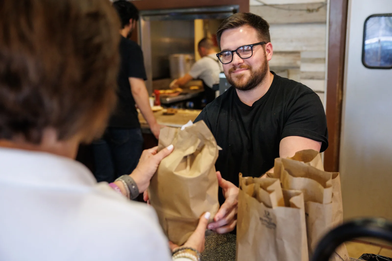 A Bagel Boyz employee handing an order to a customer across the counter